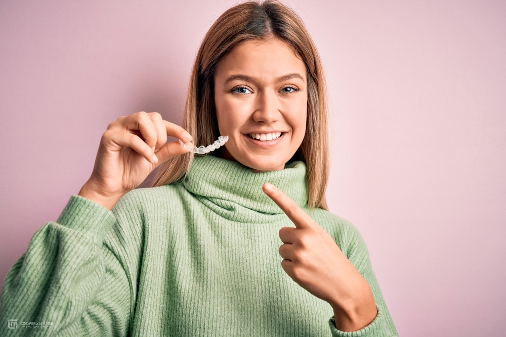 a woman pointing at her clear invsalign after comparing aligners vs braces in Tulsa, OK