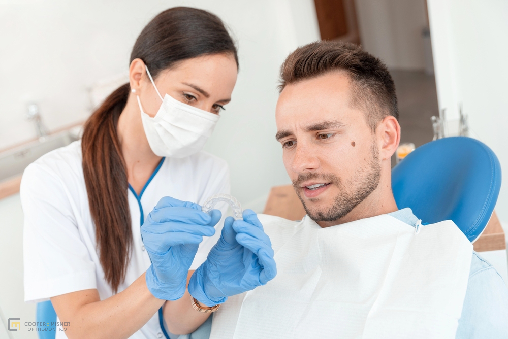 Orthodontist showing a dental appliance to a smiling male patient during a consultation after being explained about Does Insurance Cover Invisalign in Tulsa, OK