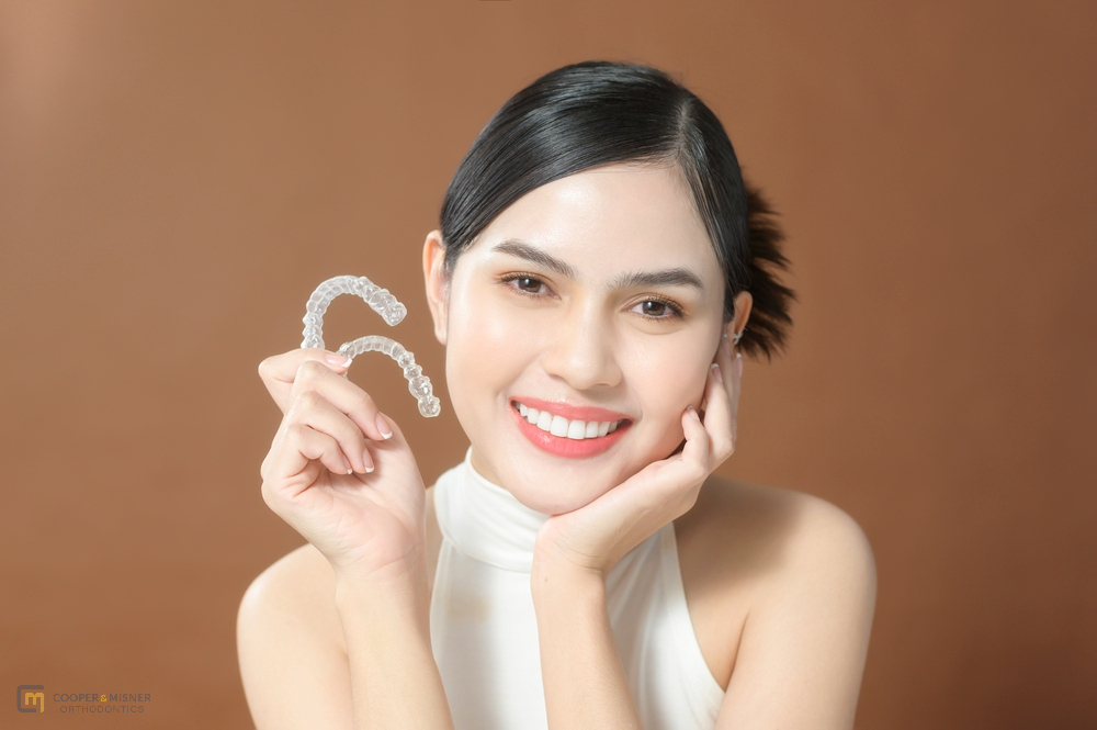 Happy young woman holding a clear aligner and smiling after understanding Does Insurance Cover Invisalign in Tulsa, OK