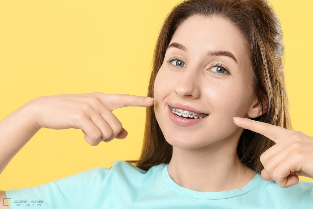 smiling woman pointing her metal braces yellow background - How to Clean Braces in Tulsa, OK 