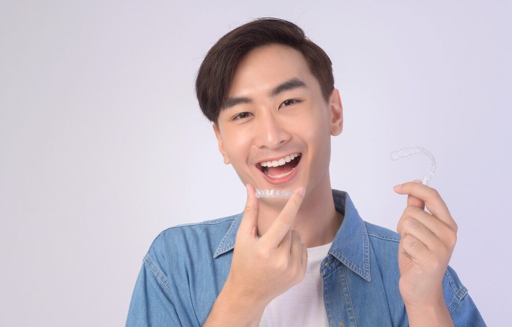 young smiling man holding invisalign clear aligners white background studio dental - How Long Does Invisalign Take in Tulsa, OK