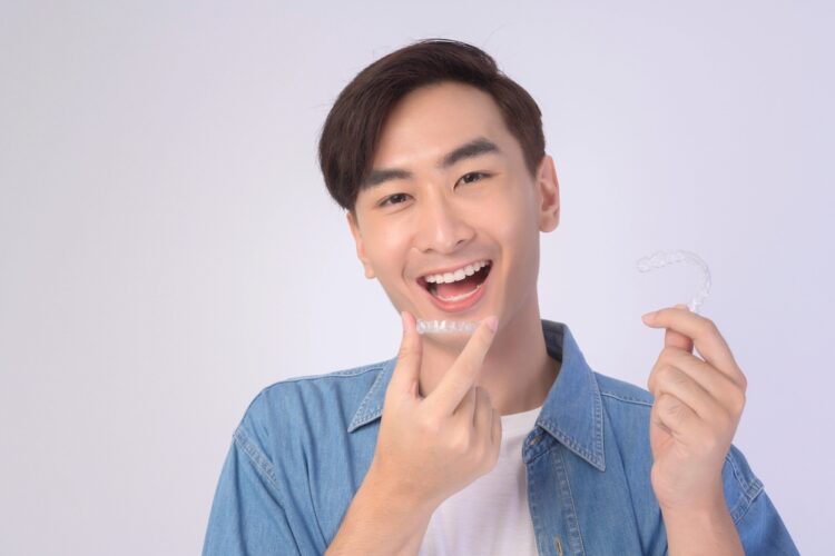 young smiling man holding invisalign clear aligners white background studio dental - How Long Does Invisalign Take in Tulsa, OK